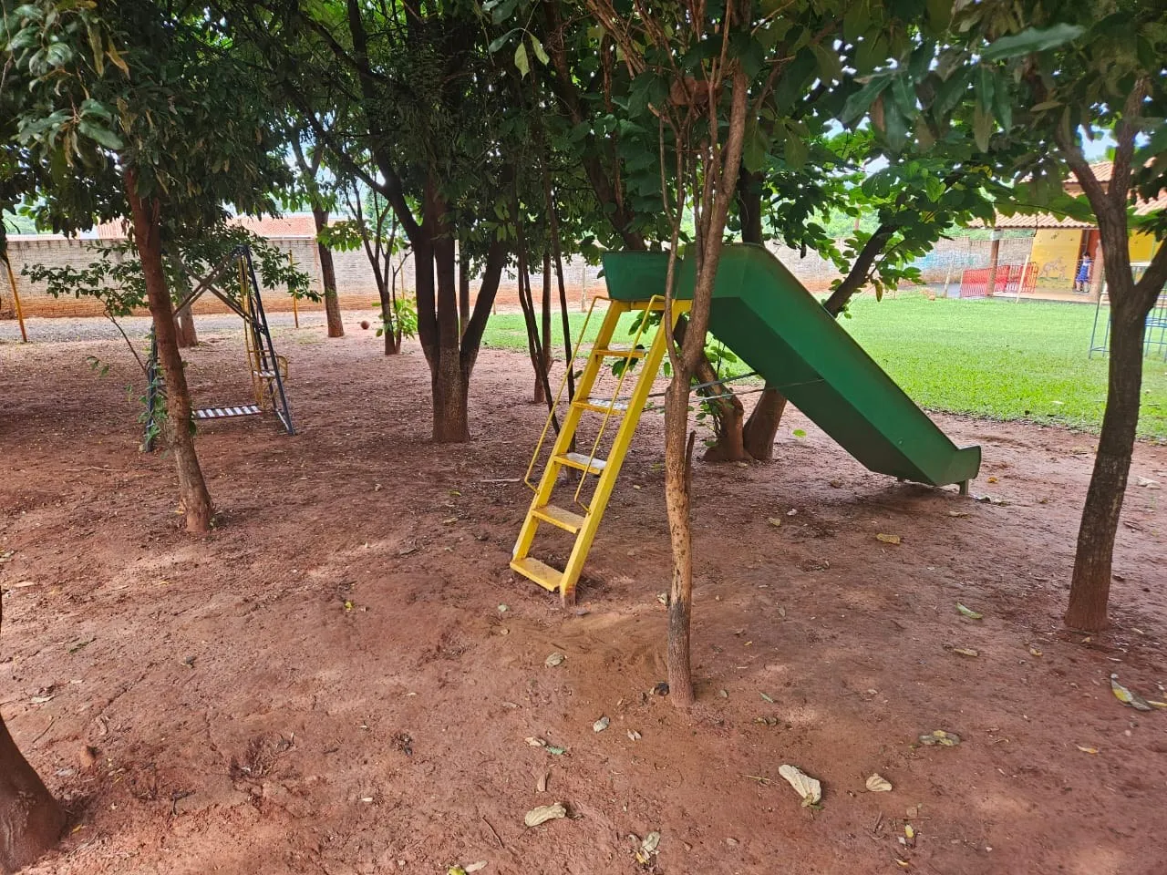 Escorregador verde com escada amarela à sombra das árvores no parque da escola
