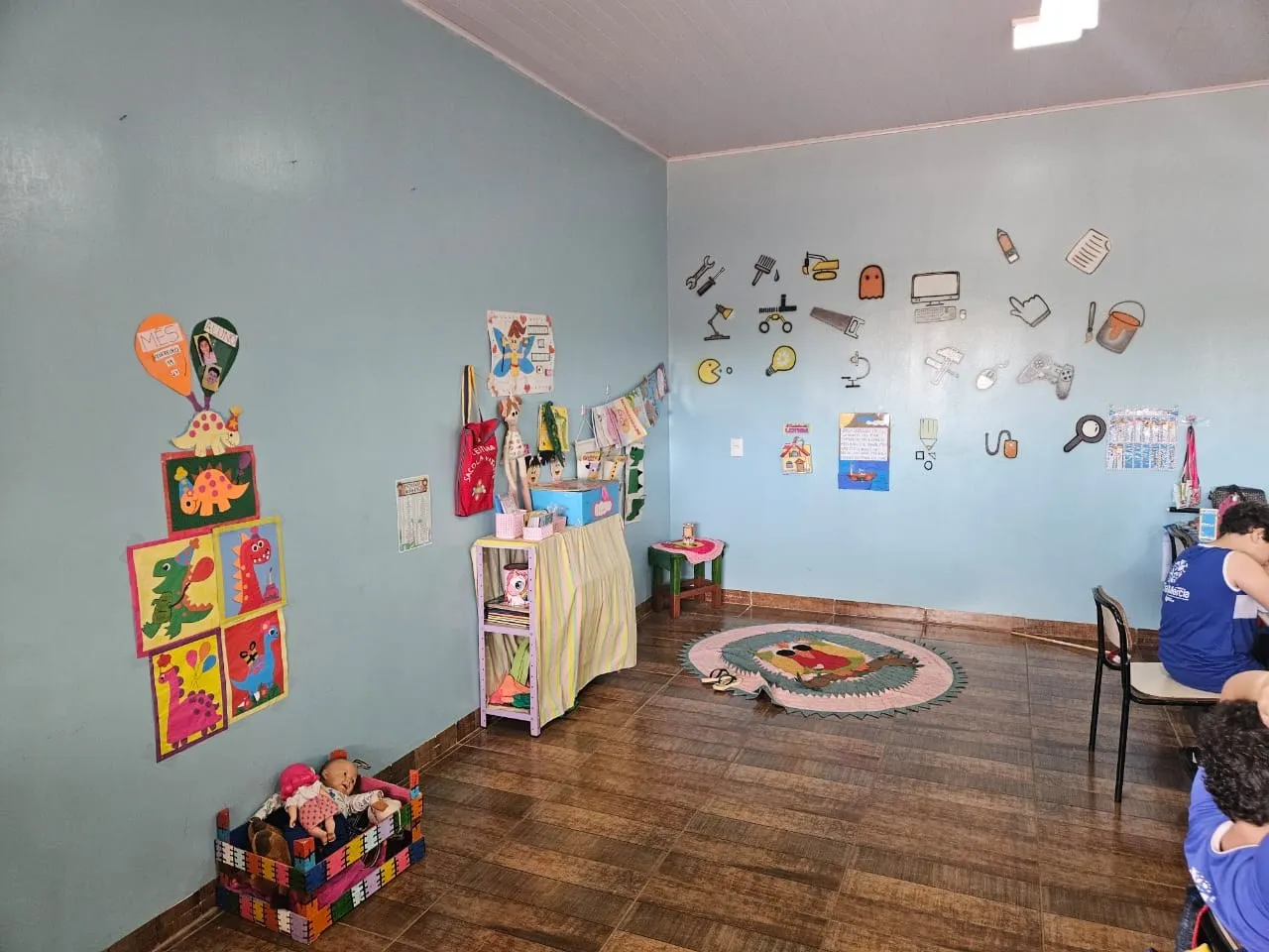 Cantinho da sala com tapete, estante de brinquedos e desenhos coloridos na parede