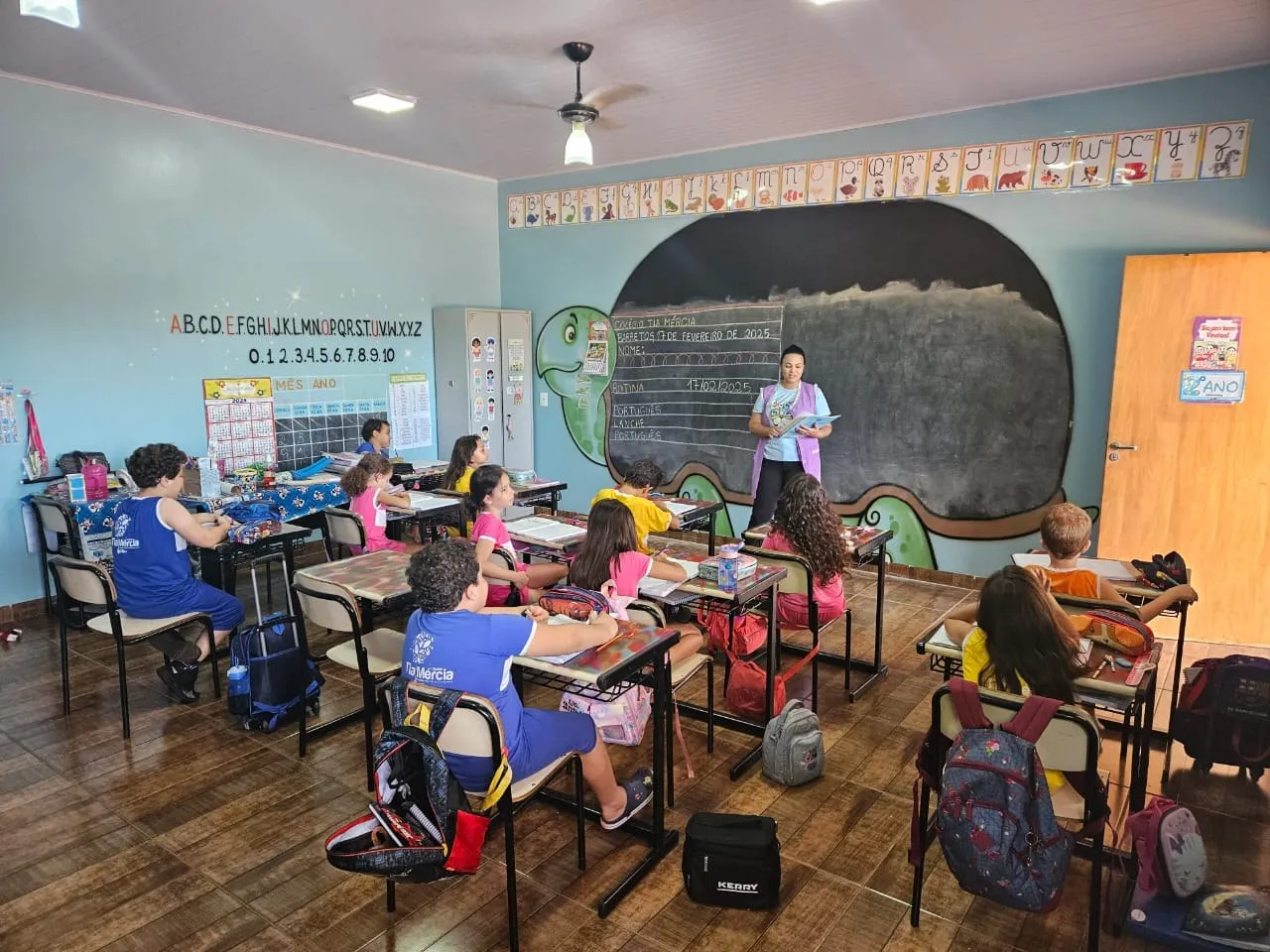 Turma em aula com a professora diante da lousa em formato de tartaruga