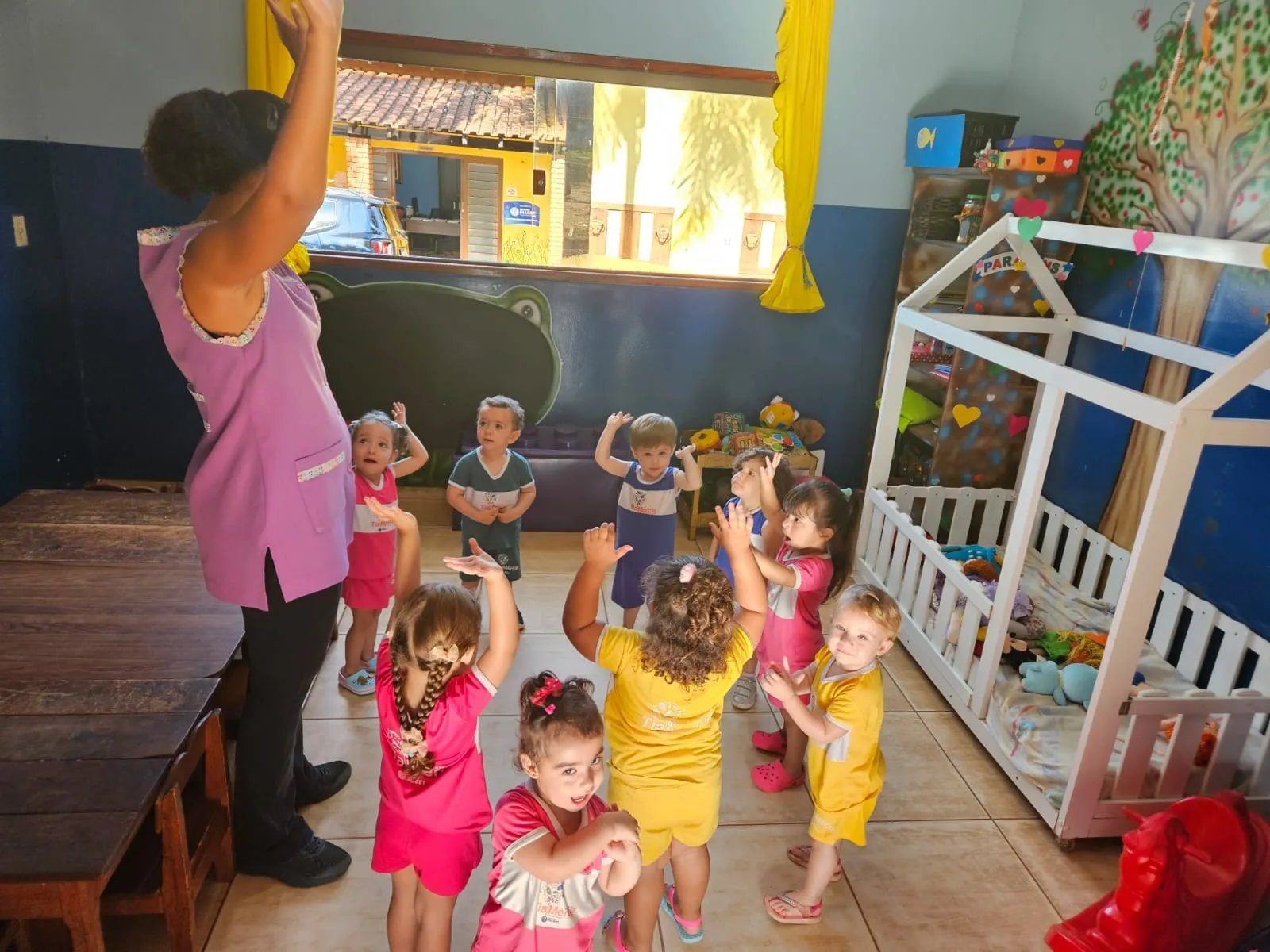 Professora e crianças pequenas dançando com os braços para o alto