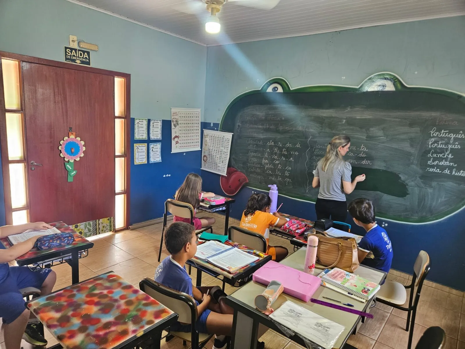 Professora escrevendo na lousa em formato de sapo, com os alunos em suas carteiras
