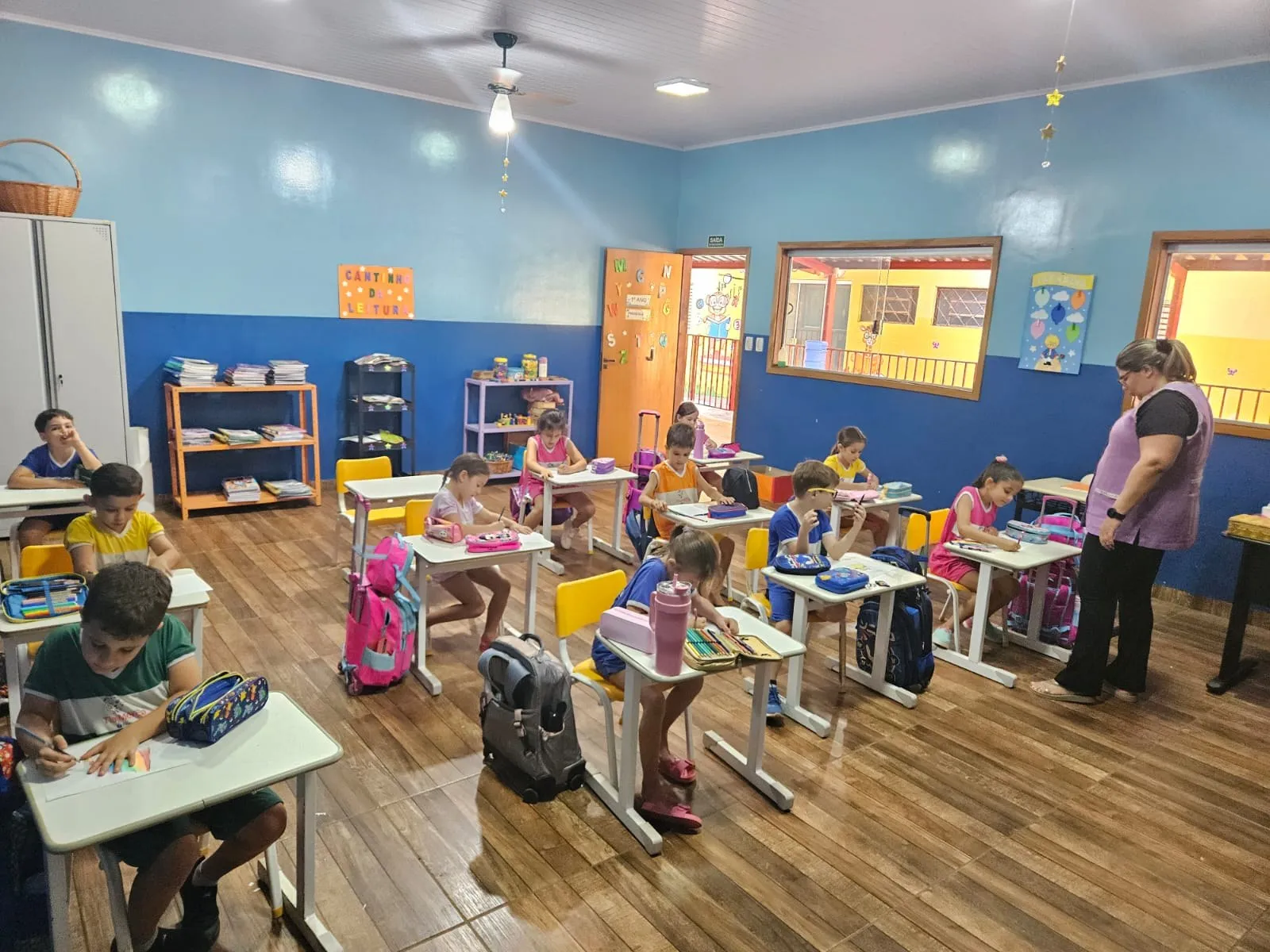Professora acompanhando os alunos, que escrevem em suas carteiras